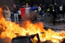 Foto: Seorang demonstran membentangkan bendera Prancis di dekat kobaran api yang membakar barikade jalanan saat aksi unjuk rasa besar-besaran menuntut penurunan biaya hidup berujung ricuh di Paris.