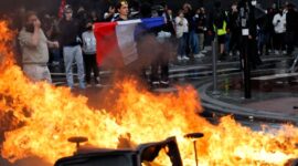 Foto: Seorang demonstran membentangkan bendera Prancis di dekat kobaran api yang membakar barikade jalanan saat aksi unjuk rasa besar-besaran menuntut penurunan biaya hidup berujung ricuh di Paris.