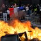 Foto: Seorang demonstran membentangkan bendera Prancis di dekat kobaran api yang membakar barikade jalanan saat aksi unjuk rasa besar-besaran menuntut penurunan biaya hidup berujung ricuh di Paris.