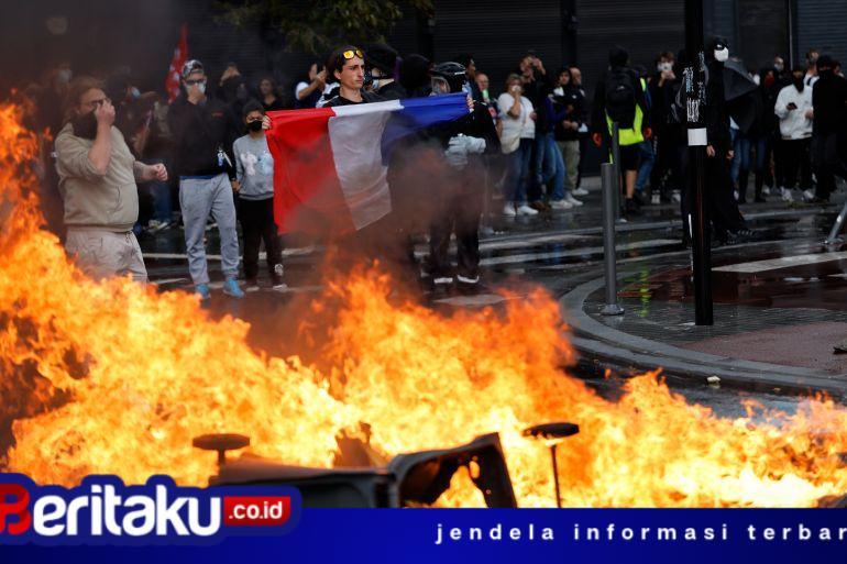 Foto: Seorang demonstran membentangkan bendera Prancis di dekat kobaran api yang membakar barikade jalanan saat aksi unjuk rasa besar-besaran menuntut penurunan biaya hidup berujung ricuh di Paris.